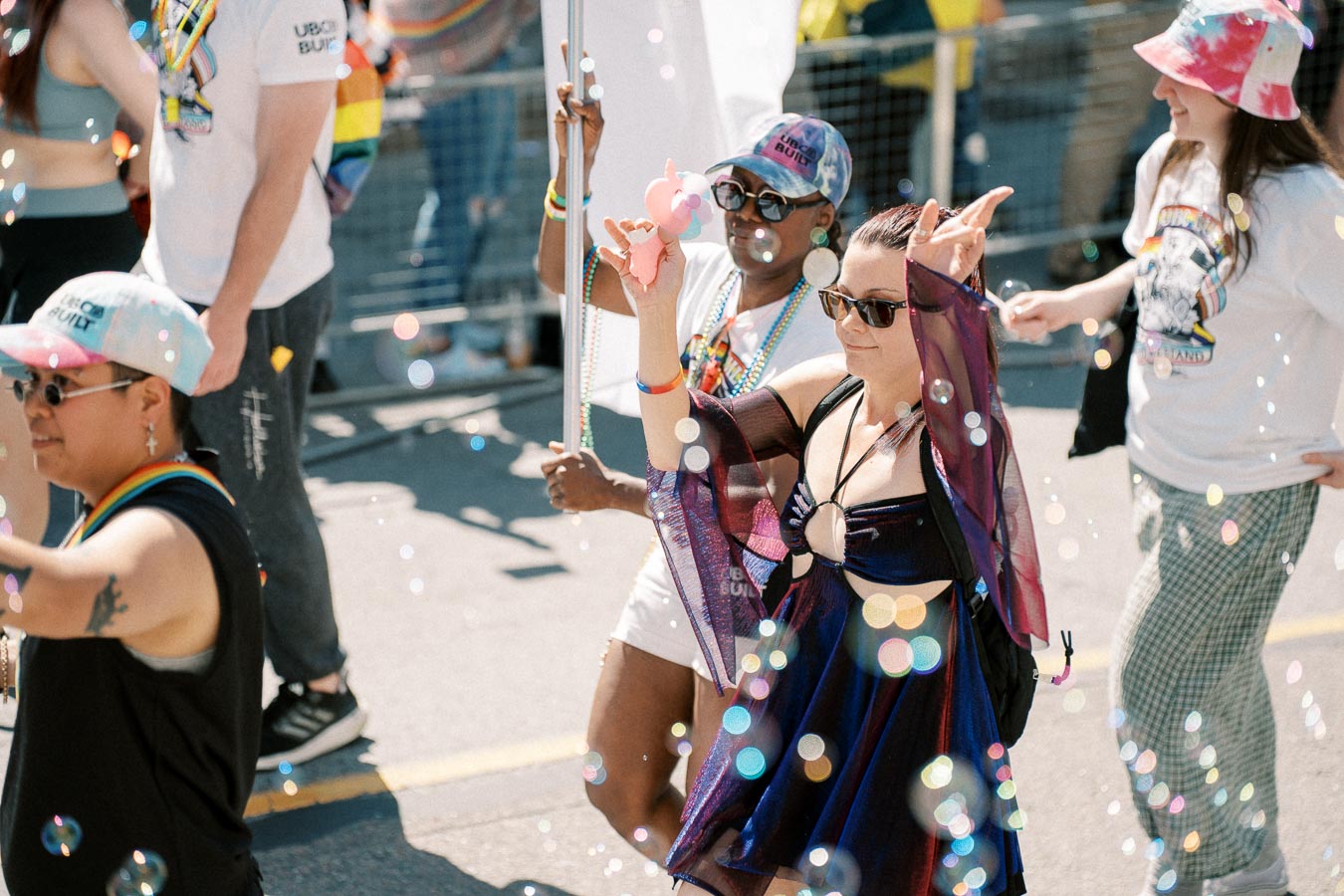 Participants in a pride parade celebrate with colorful outfits and bubbles, creating a festive atmosphere.