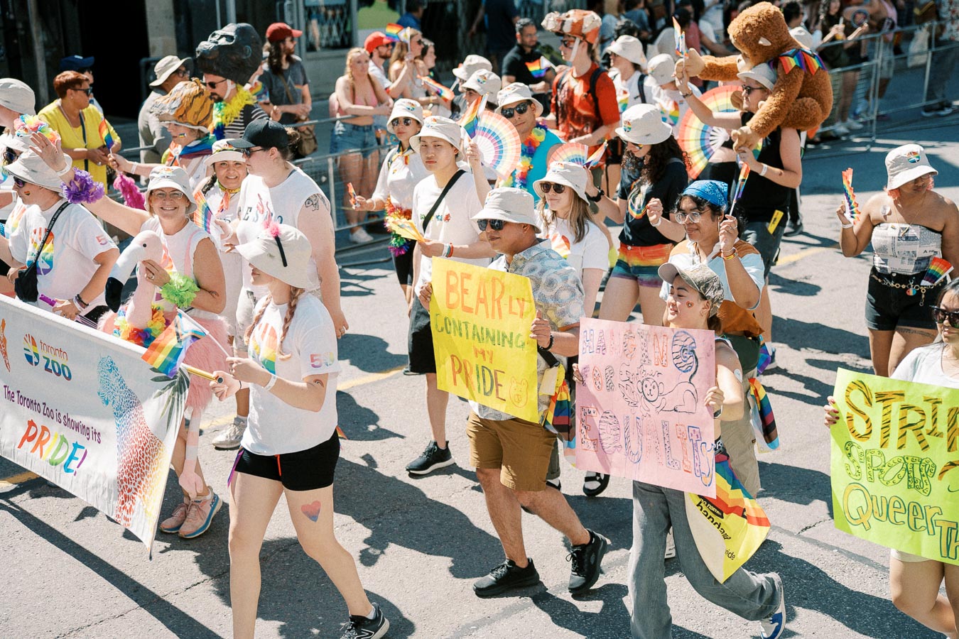 Participants in a Pride parade hold colorful signs and a Toronto Zoo banner, celebrating diversity and inclusion.