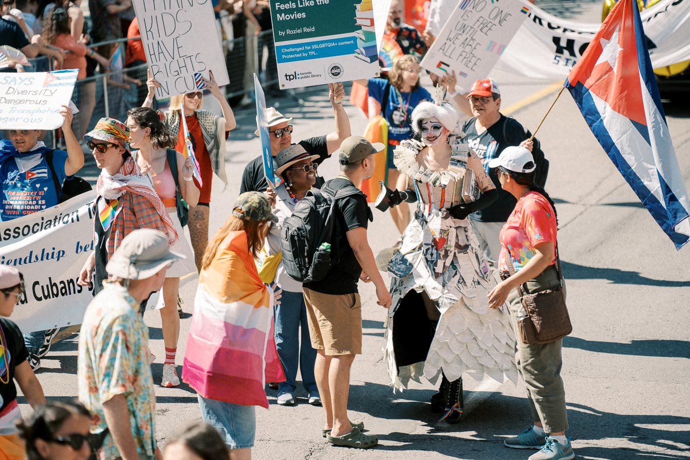 Participants in a parade hold signs advocating for rights and equality, with one person wearing a unique paper costume.