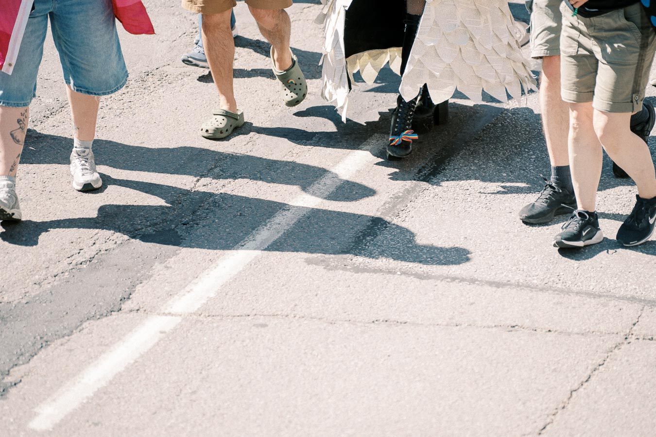A group of people walking on a street, featuring a variety of footwear including casual shoes and a costume with feather-like details.