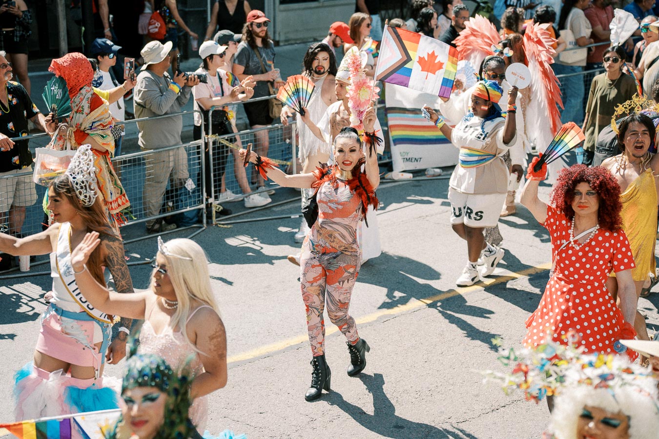 Participants in colorful costumes celebrate at a vibrant parade, waving rainbow flags and fans, symbolizing diversity and inclusion.