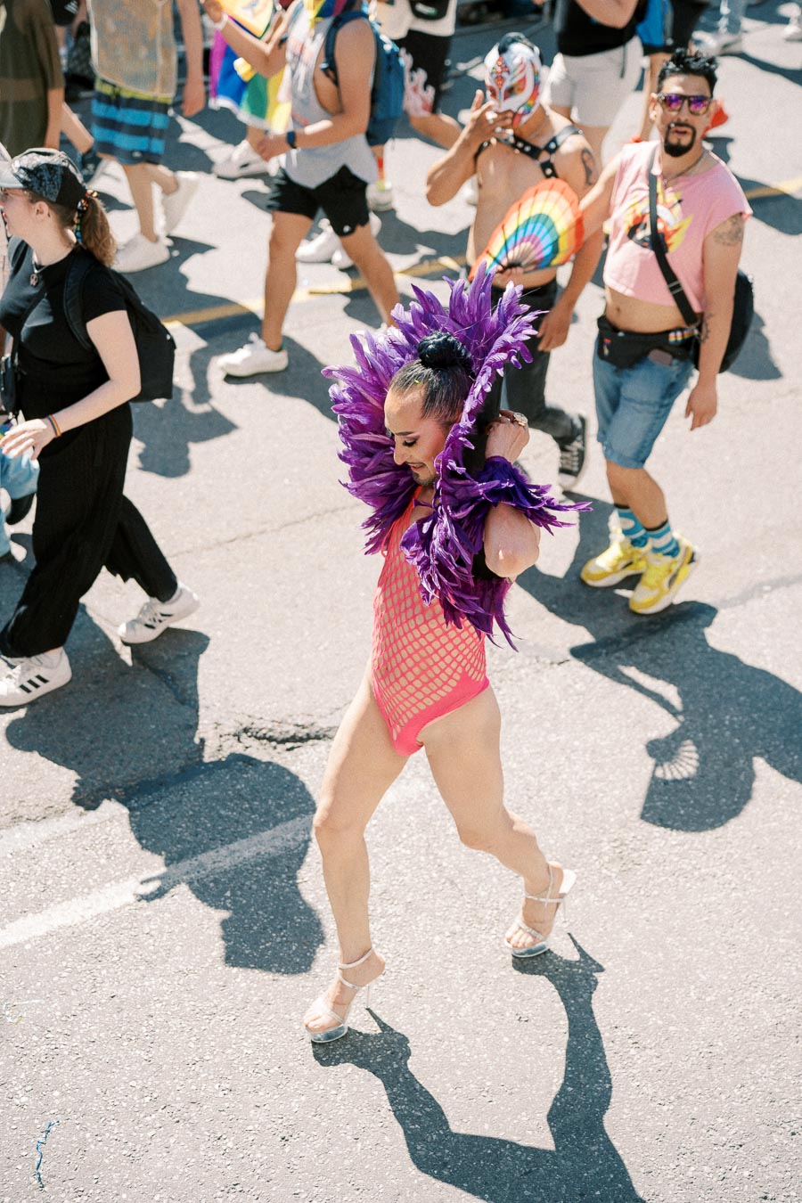 A participant in a colorful outfit walks in a lively parade, surrounded by others in festive attire.