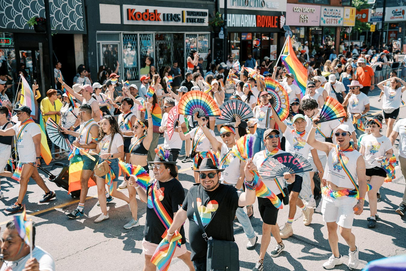 Participants joyfully march in a Pride parade, showcasing vibrant rainbow flags and fans, celebrating diversity and inclusion.