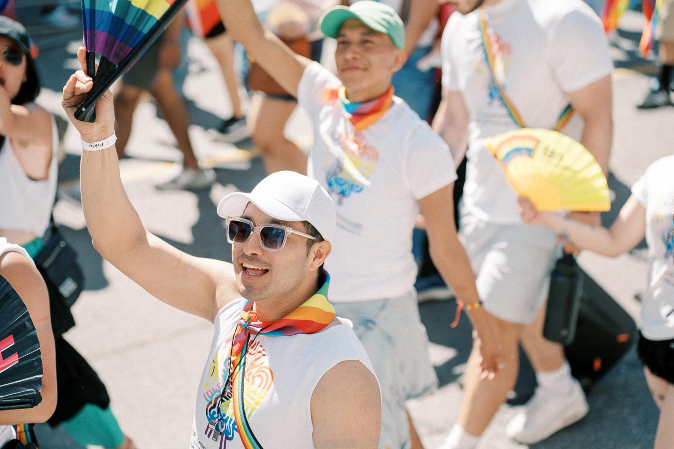 Participants at a pride parade joyfully wave rainbow fans and wear colorful accessories, celebrating diversity and inclusion.