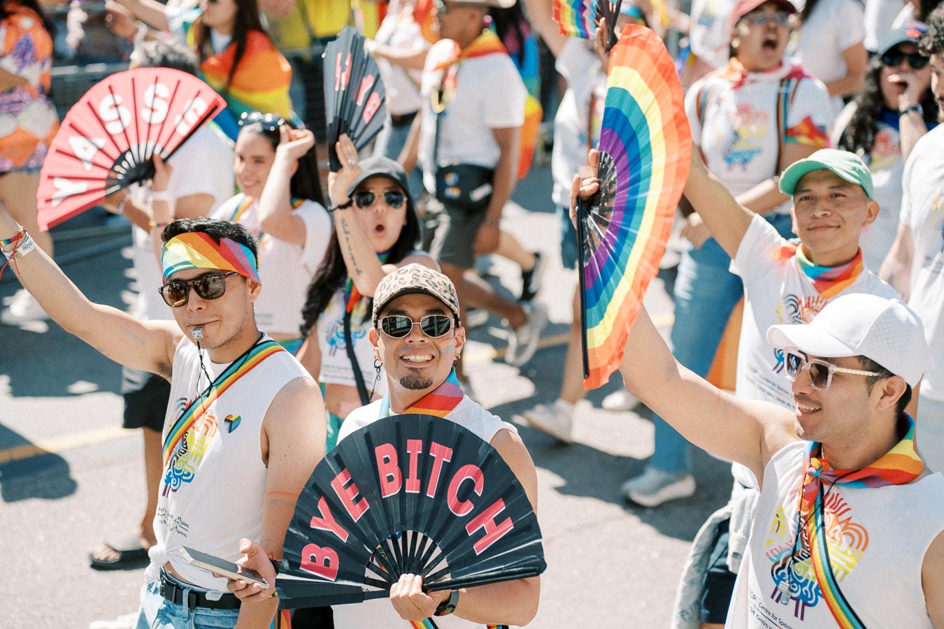 Participants at a pride parade joyfully wave colorful fans and wear rainbow-themed attire, celebrating diversity and inclusion.