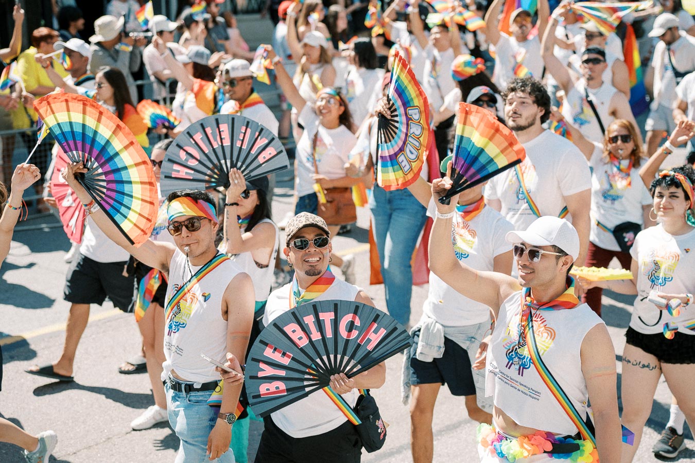 Participants at a pride parade celebrate with rainbow-themed accessories and fans, showcasing vibrant expressions of support and inclusivity.