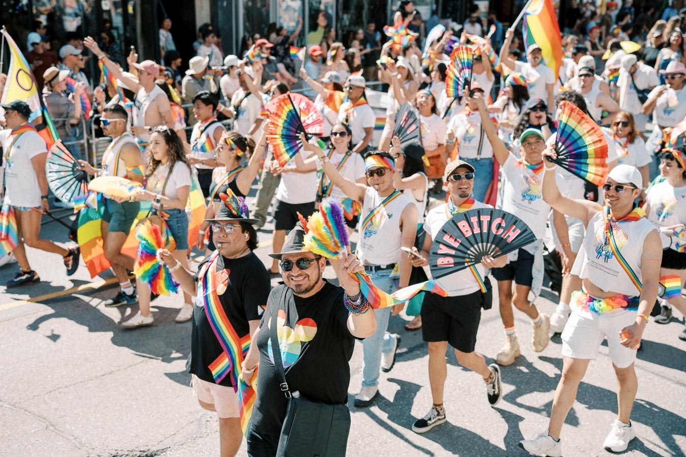 Participants at a Pride parade joyfully wave rainbow flags and fans, celebrating diversity and inclusion.