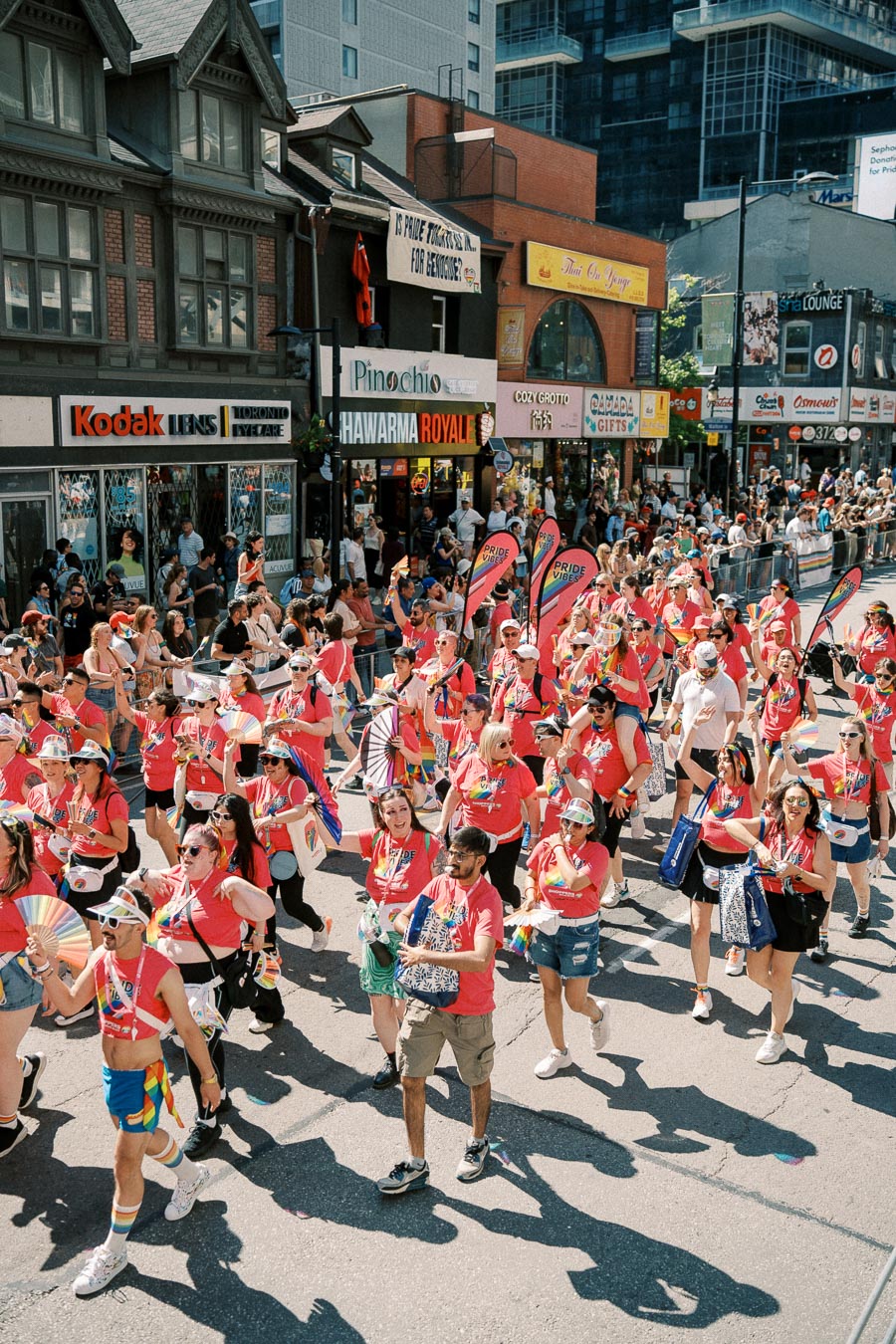 Participants in a vibrant street parade wearing pink shirts and carrying rainbow flags, celebrating diversity and inclusion in an urban setting.
