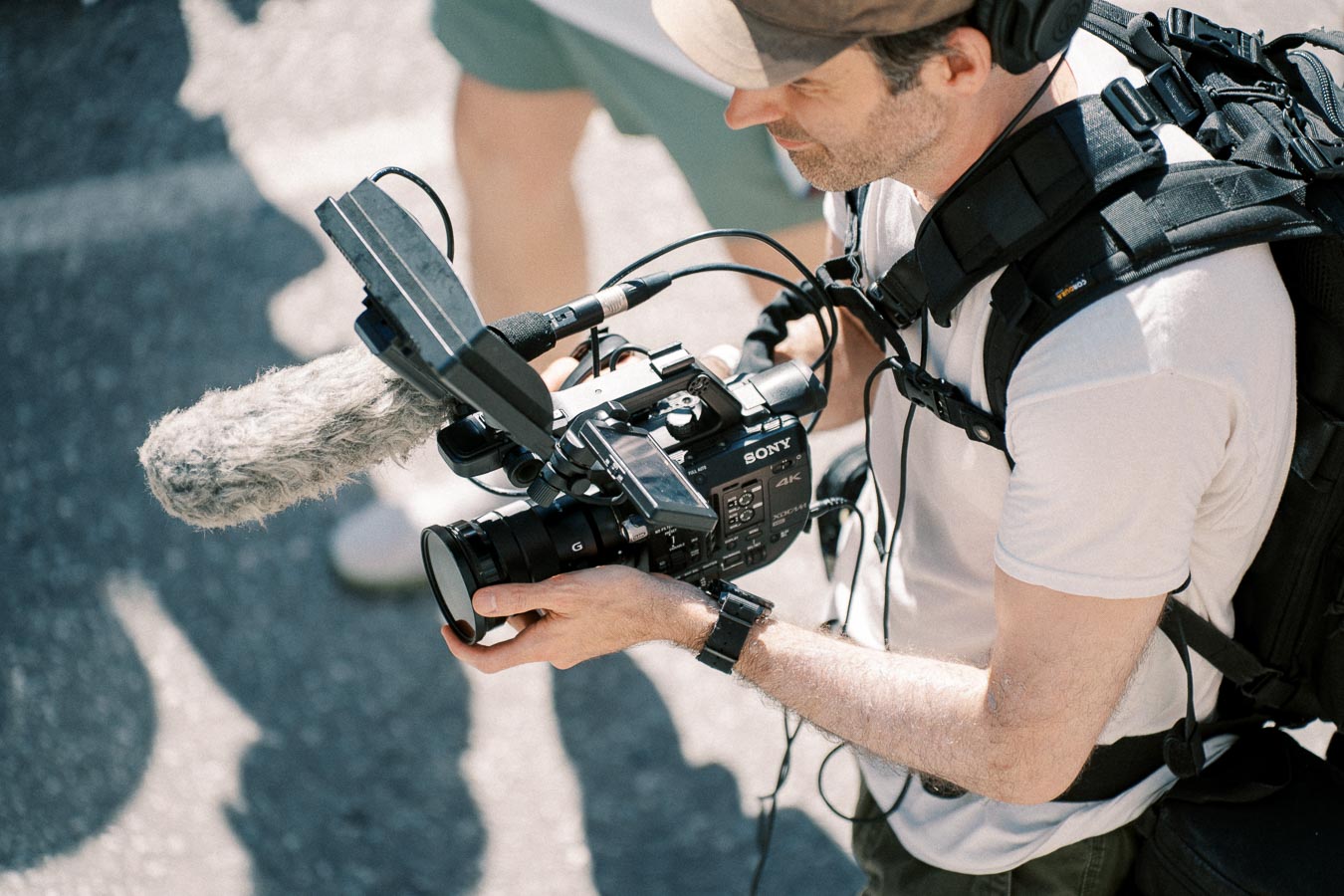 A videographer using a Sony camera with a microphone attachment, capturing footage outdoors.