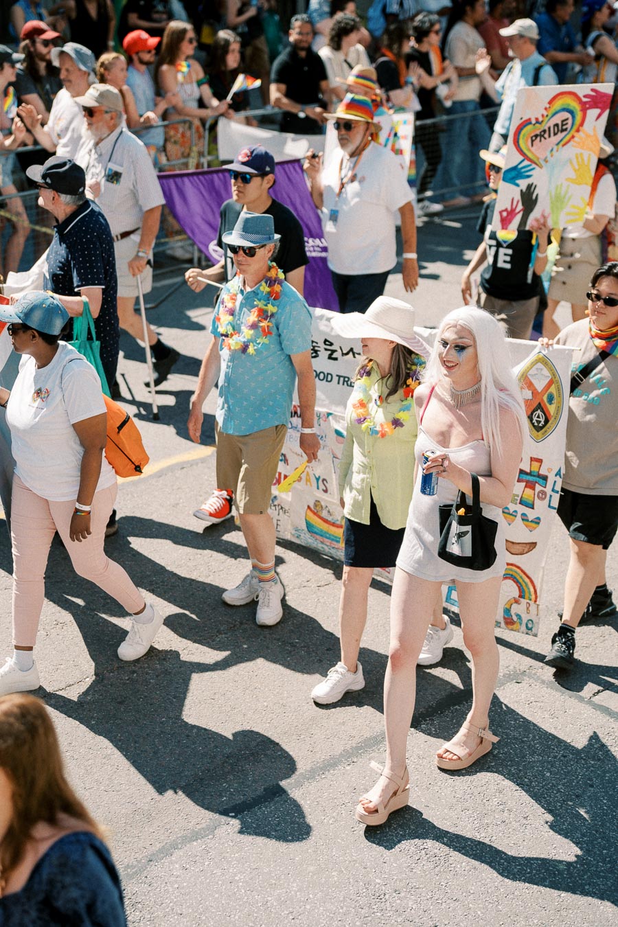Participants in a pride parade wearing colorful outfits and accessories, holding banners with rainbow designs and messages of inclusivity.