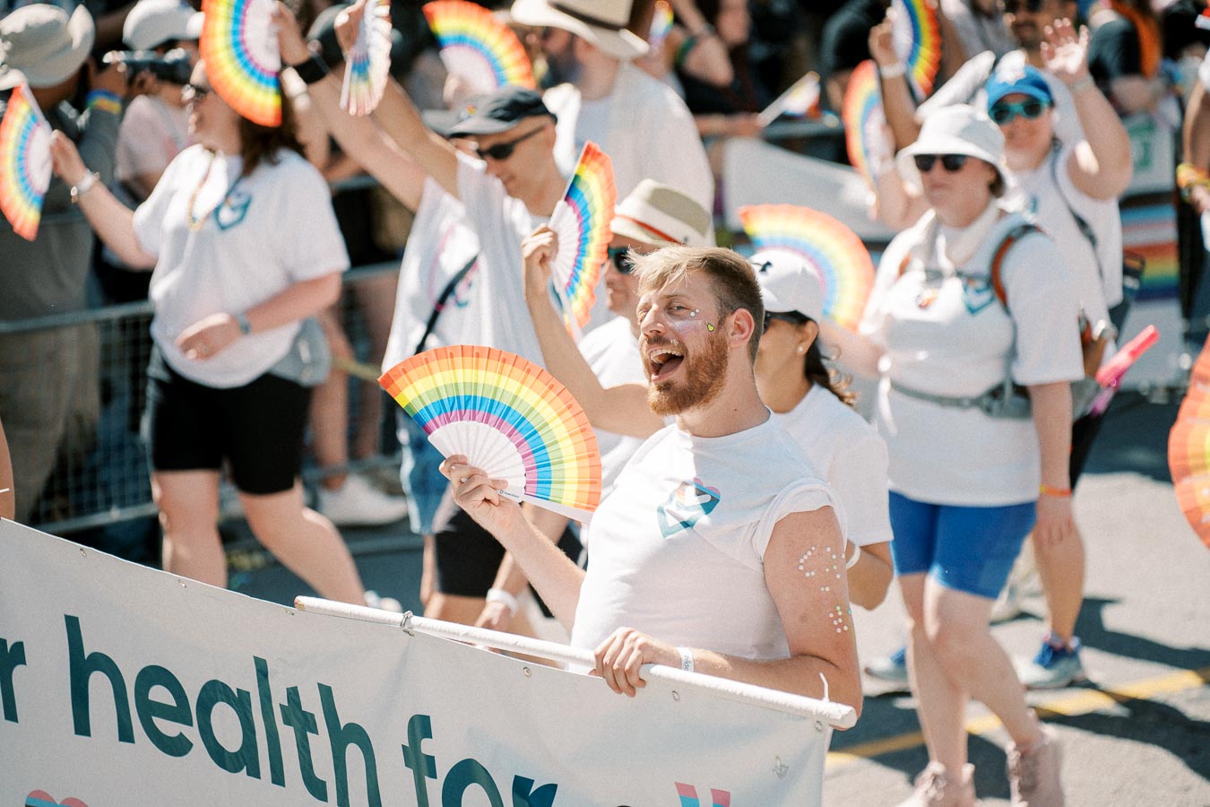 Participants in a pride parade joyfully wave rainbow fans, celebrating diversity and inclusion.