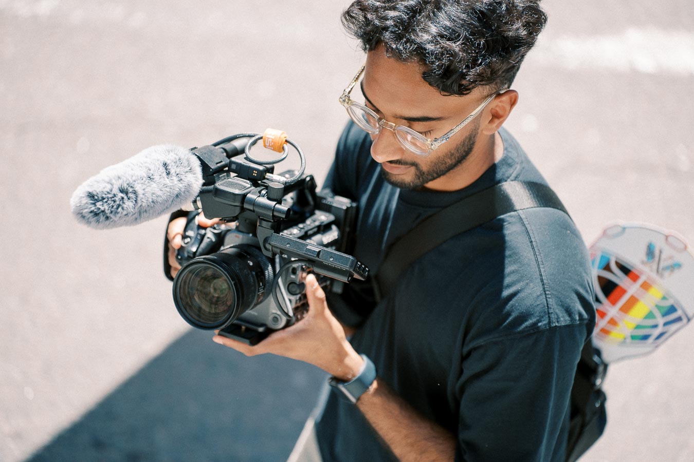 A person operating a professional video camera with an attached microphone, captured in an outdoor setting.