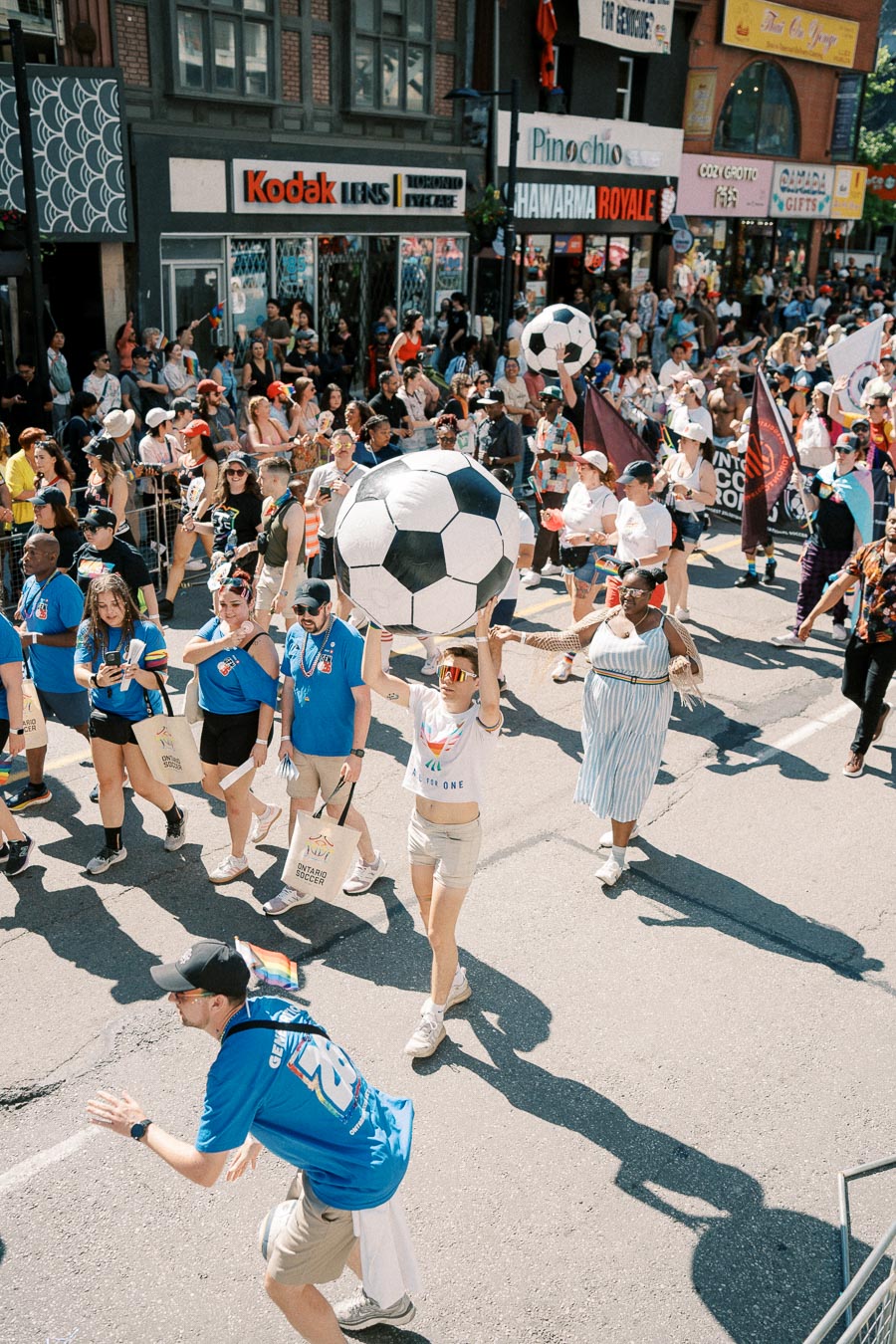 Participants in a vibrant parade carry large soccer balls, celebrating diversity and community spirit on a bustling city street.