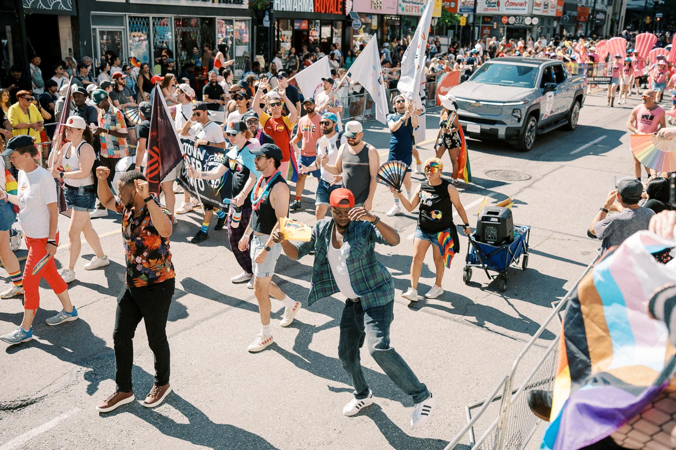 Participants in a vibrant street parade celebrate with flags, banners, and colorful outfits, creating a festive atmosphere.