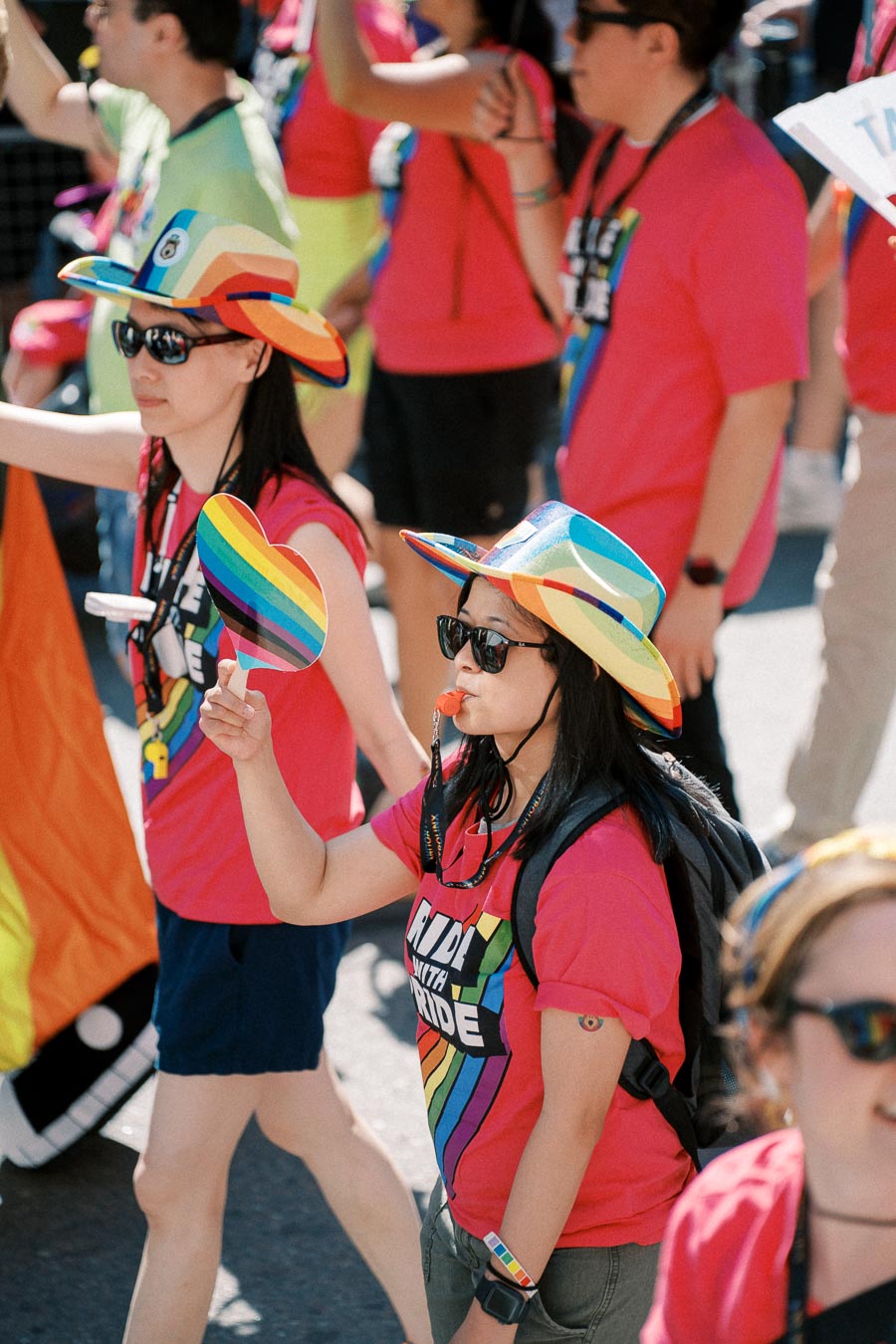 Participants in a pride parade wearing colorful rainbow hats and holding rainbow flags, celebrating diversity and inclusion.