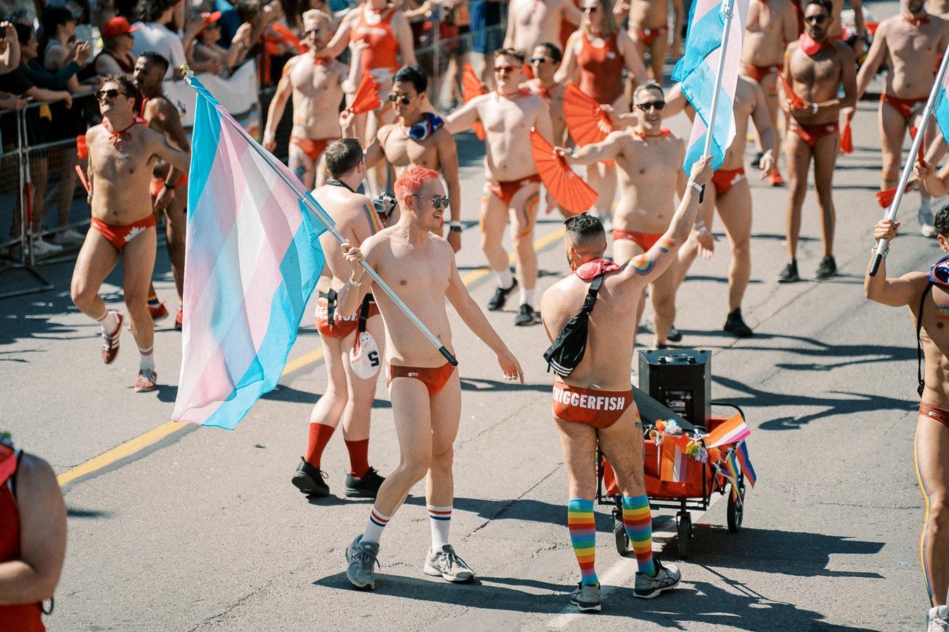 Participants in a pride parade wearing red swimwear and holding flags, celebrating diversity and inclusion.