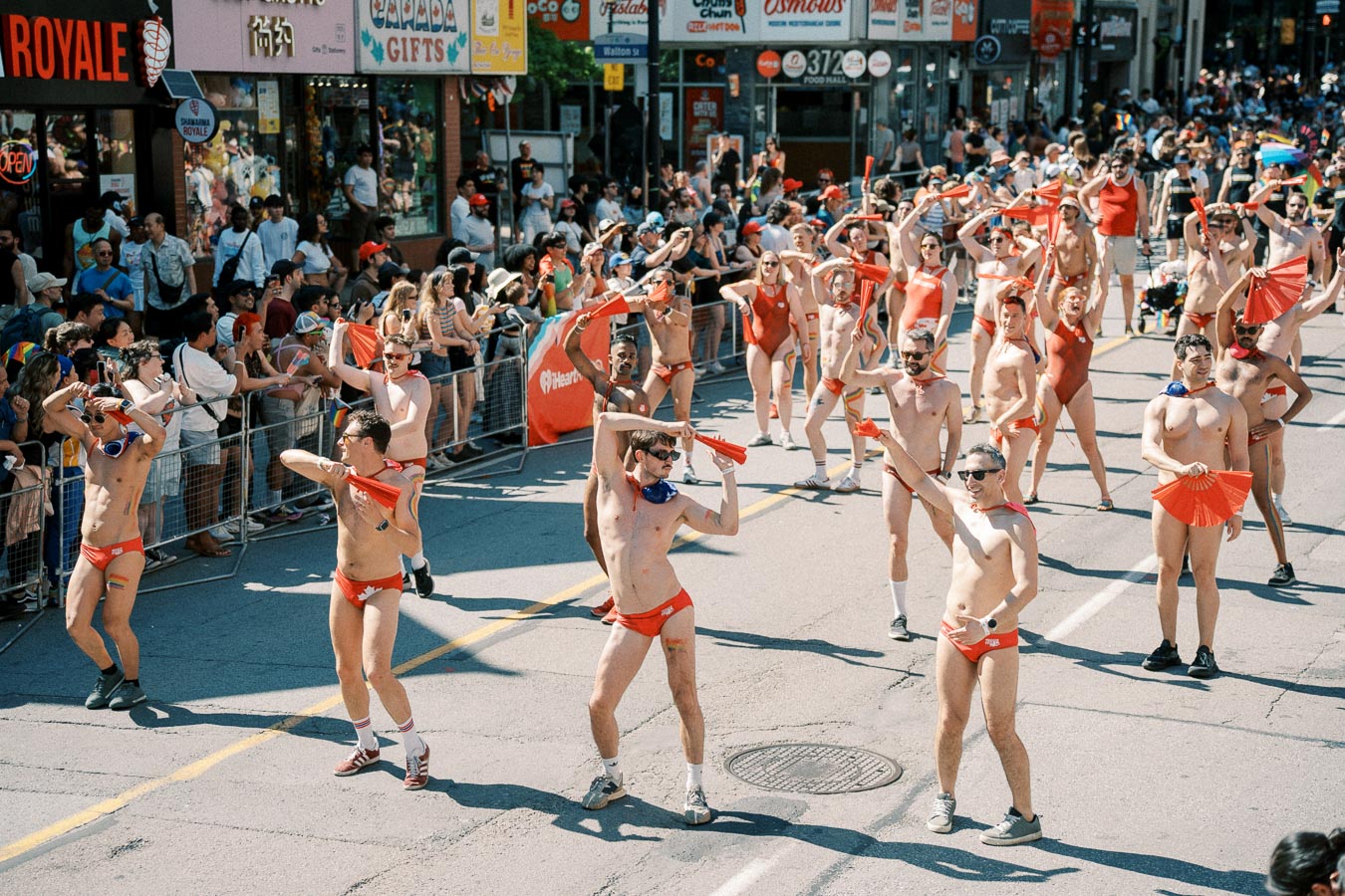 Participants in red swimwear dance energetically during a parade, with spectators lining the street.