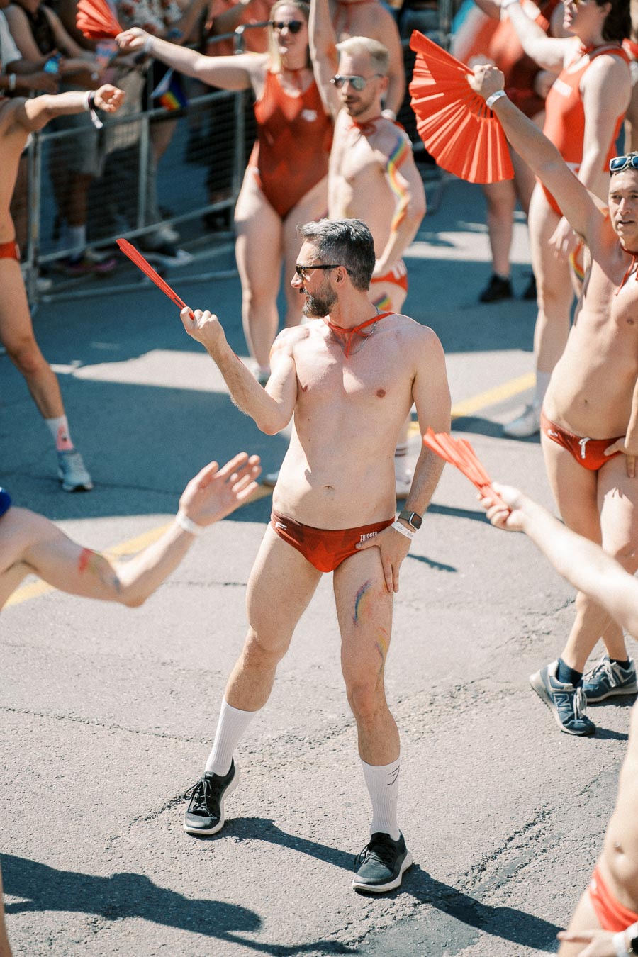 Participants in a parade wearing red swimwear and holding red fans, celebrating with enthusiasm.
