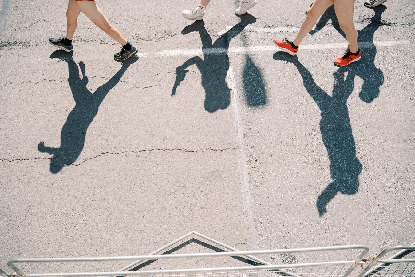 Shadows of people walking on a sunny street, highlighting their legs and shoes.