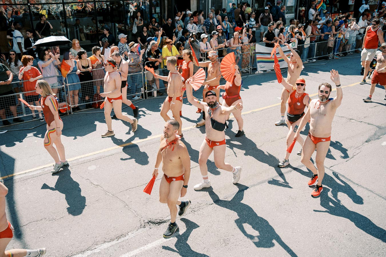 Participants in red swimwear and accessories march in a lively parade, engaging with the cheering crowd.