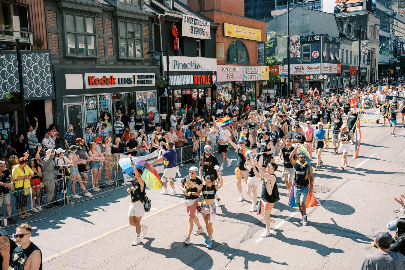 A lively parade featuring participants with rainbow flags and umbrellas, celebrating diversity and inclusion on a bustling city street.