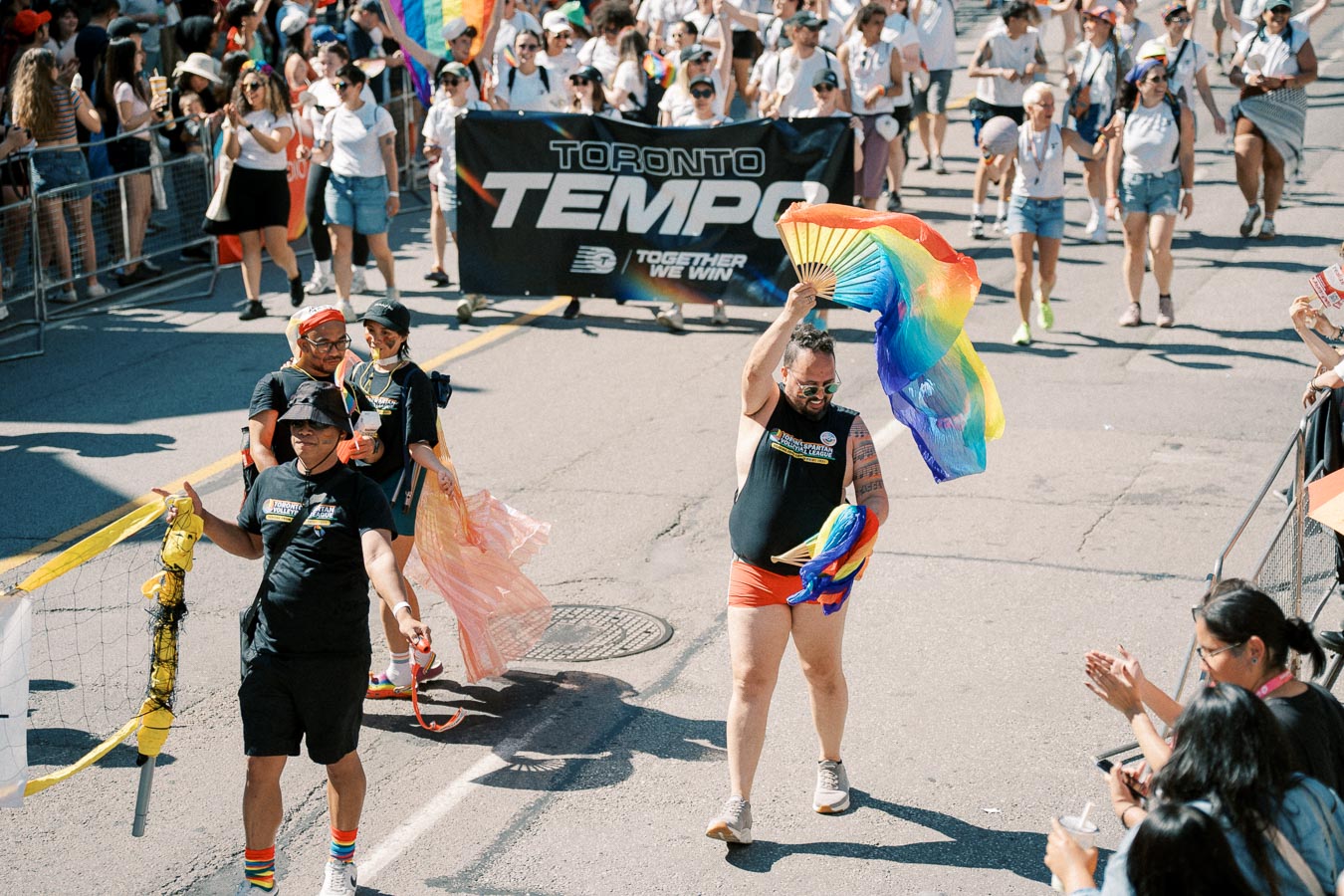 Participants in a pride parade celebrate with rainbow flags and banners, while a crowd cheers them on.