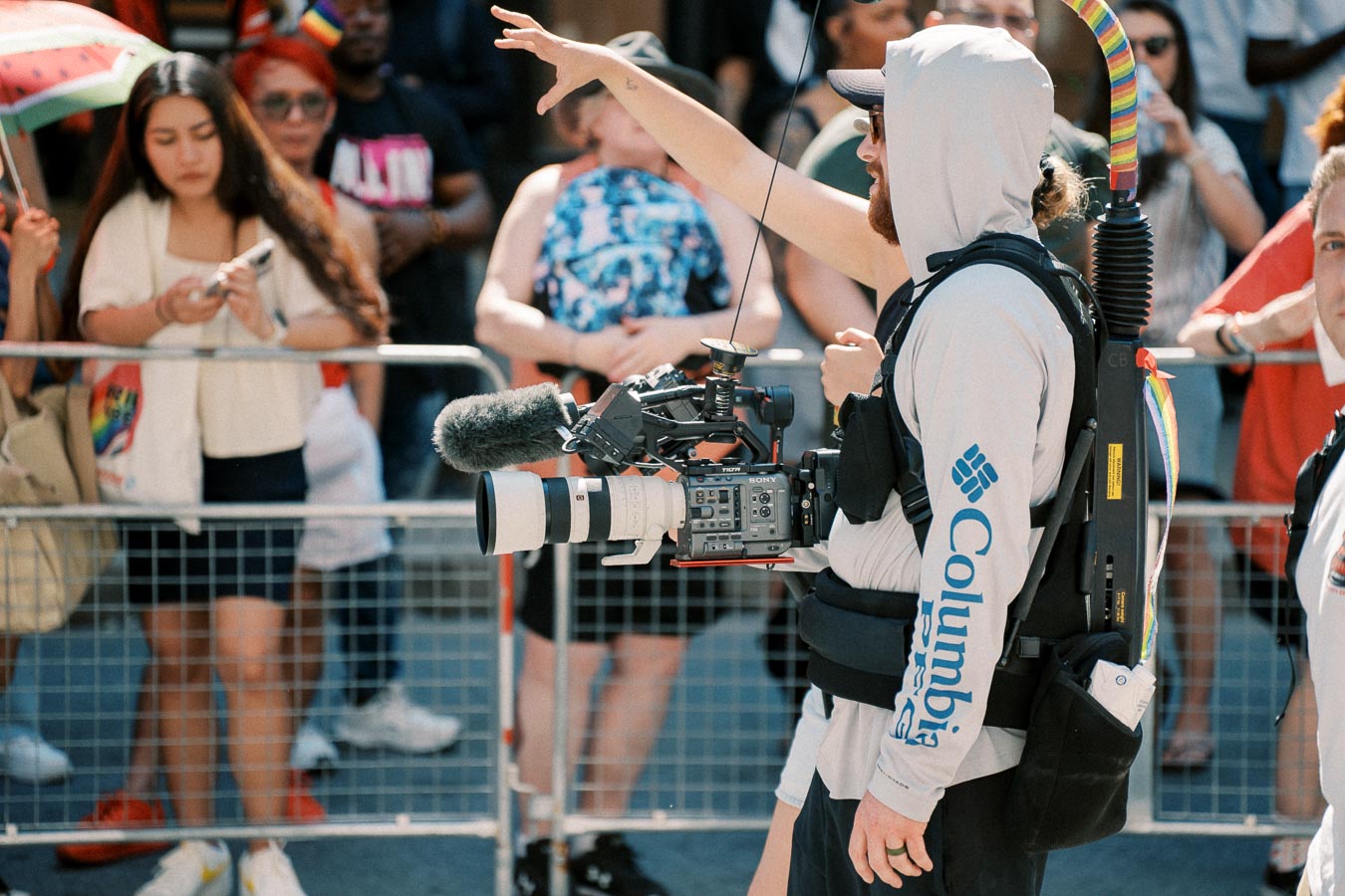 A videographer captures footage at an outdoor event, surrounded by a crowd.