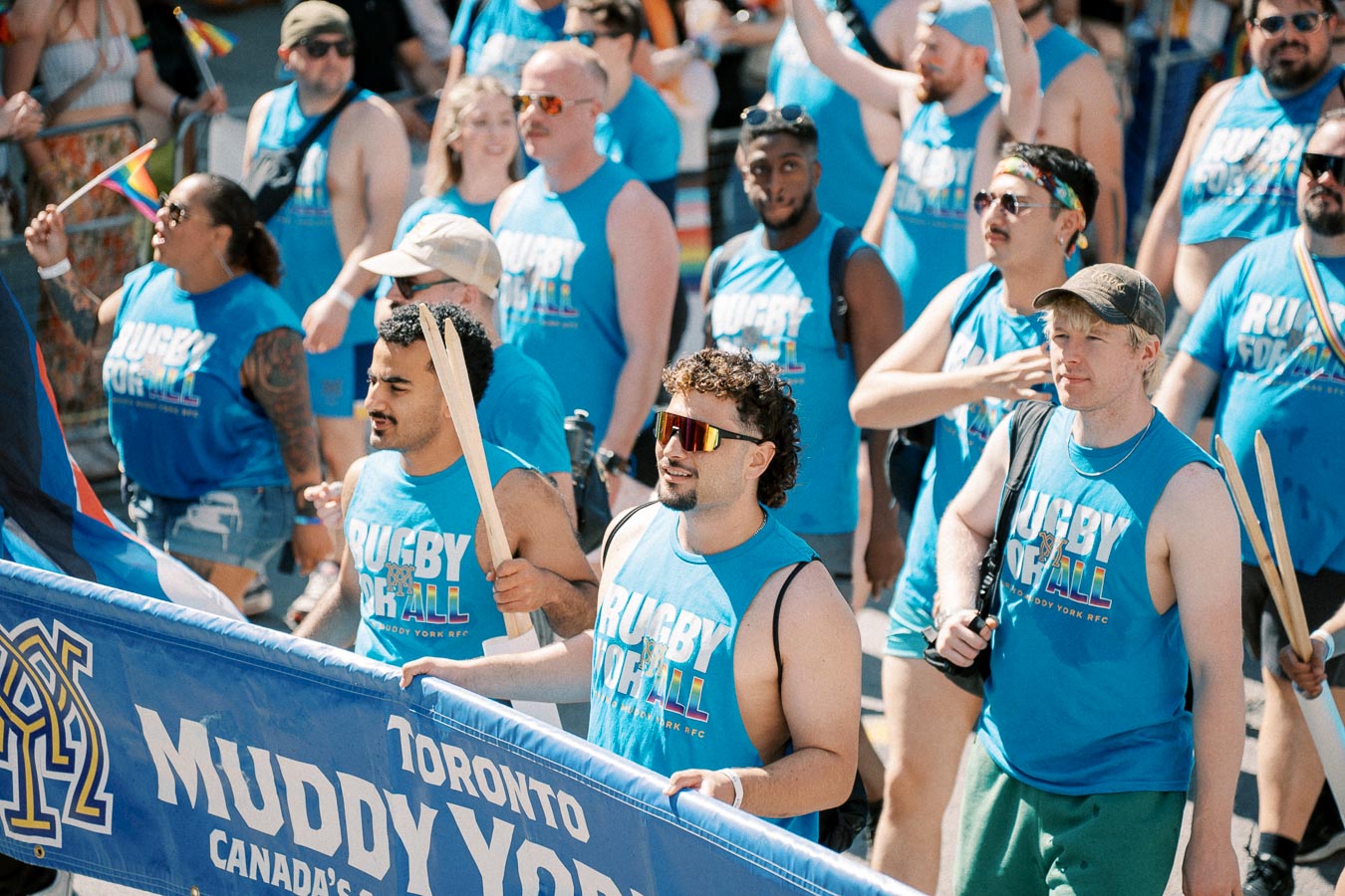 Participants in a parade wearing 'Rugby For All' shirts, representing Toronto Muddy York RFC, celebrate inclusivity and diversity.