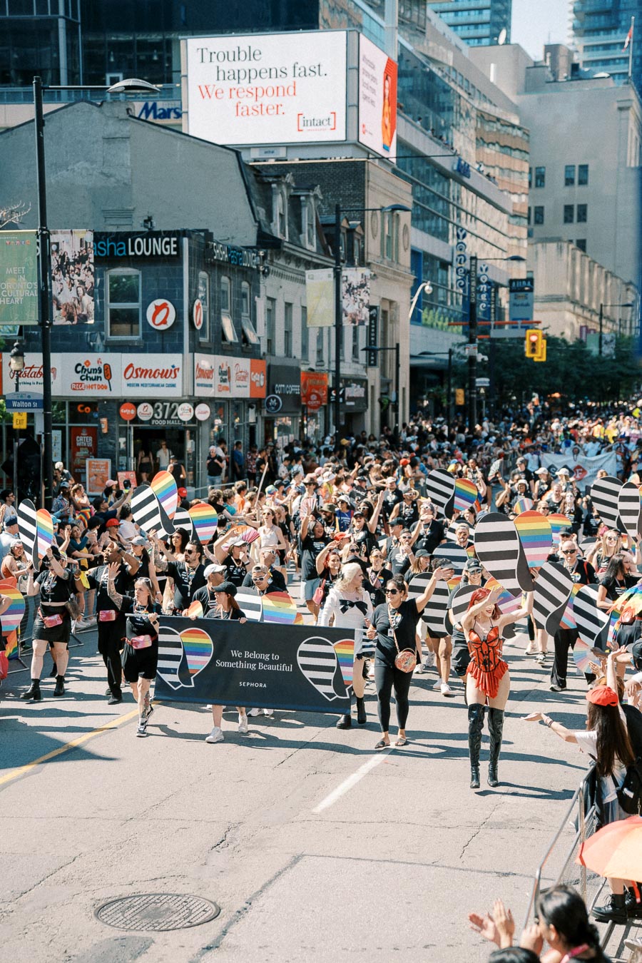 Participants in a colorful parade march down a city street, holding rainbow-themed signs and a banner from Sephora, celebrating diversity and inclusion.
