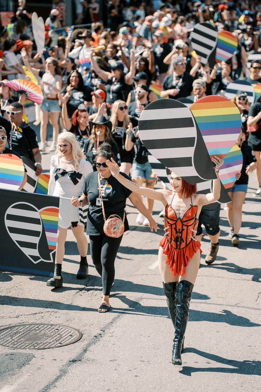 Participants in a colorful parade celebrate diversity and inclusion, holding rainbow heart signs and wearing festive attire.