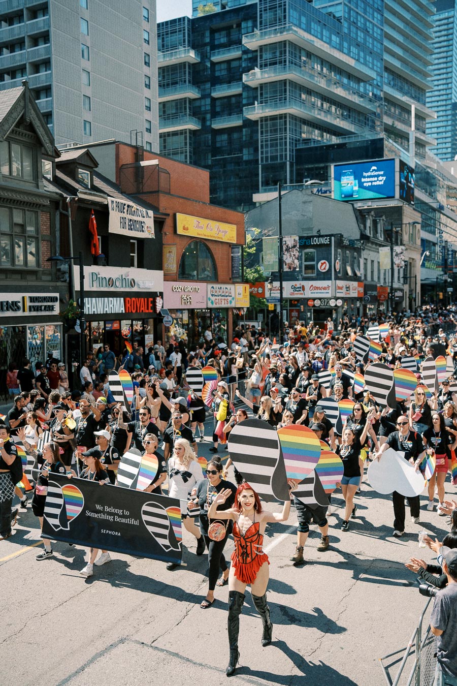 Participants in a colorful parade march down a city street, holding rainbow-themed signs and banners, celebrating diversity and inclusion.