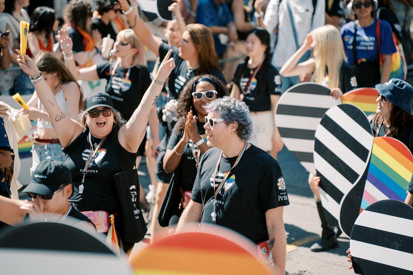 Participants at a Pride parade joyfully celebrate, holding rainbow-themed signs and wearing shirts with rainbow logos.