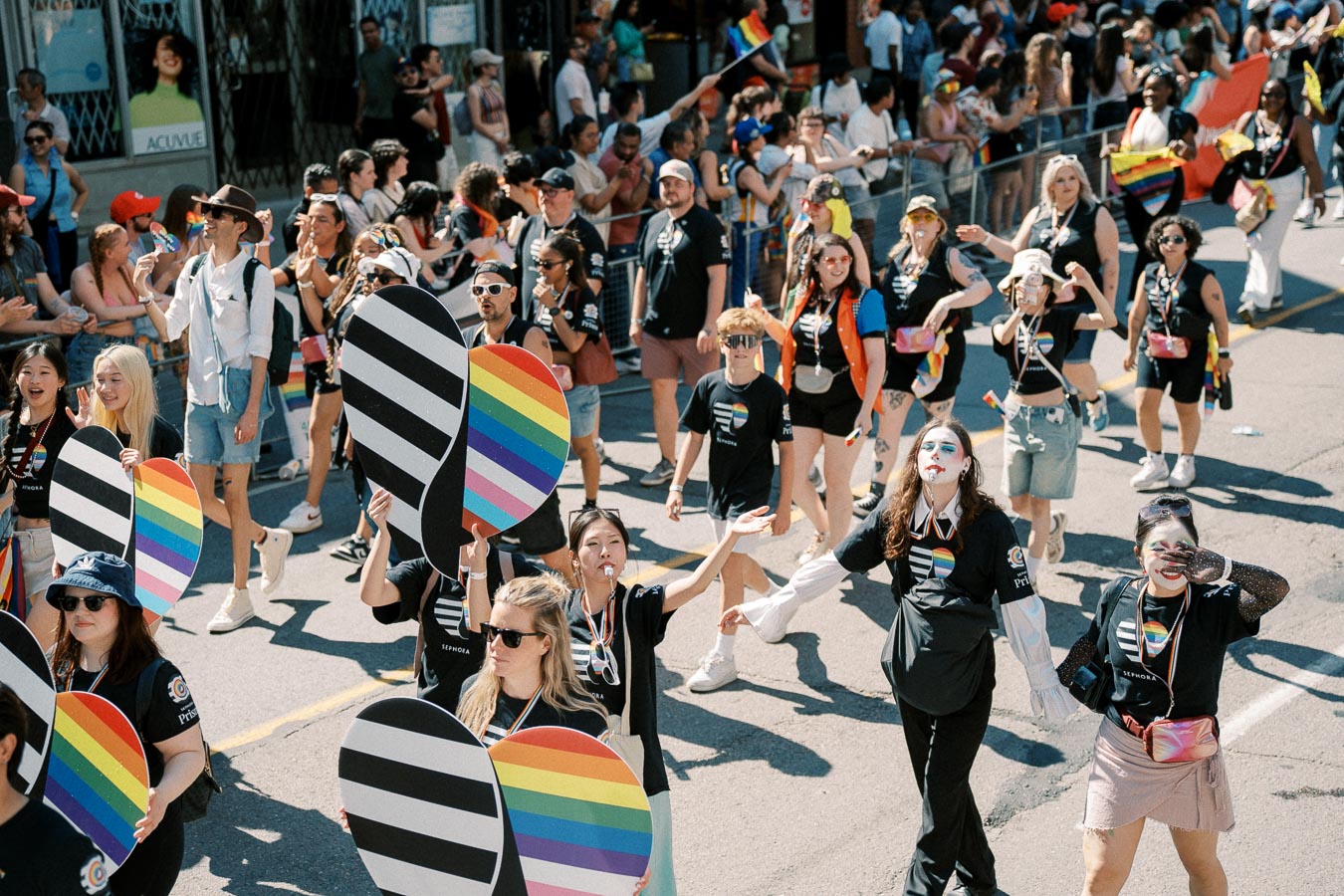 Participants in a pride parade march with rainbow-themed signs and attire, celebrating diversity and inclusion.