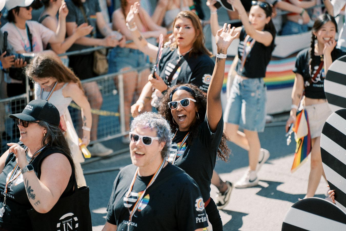 Participants in a pride parade joyfully wave to the crowd, showcasing their support with rainbow-themed attire and accessories.