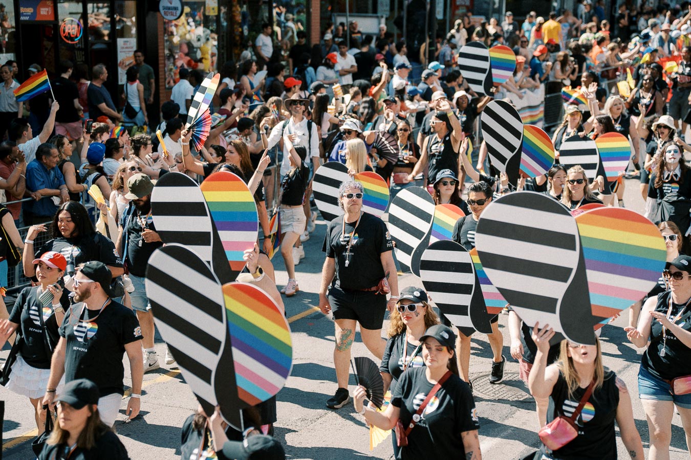 Participants in a pride parade hold rainbow-colored signs and wear matching black shirts with rainbow designs, celebrating diversity and inclusion.