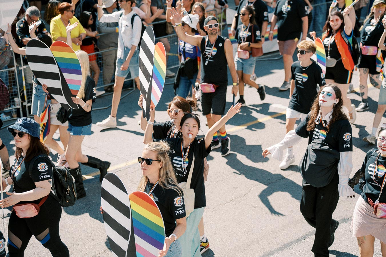 Participants in a pride parade hold rainbow-themed signs and wear shirts with rainbow designs, celebrating diversity and inclusion.