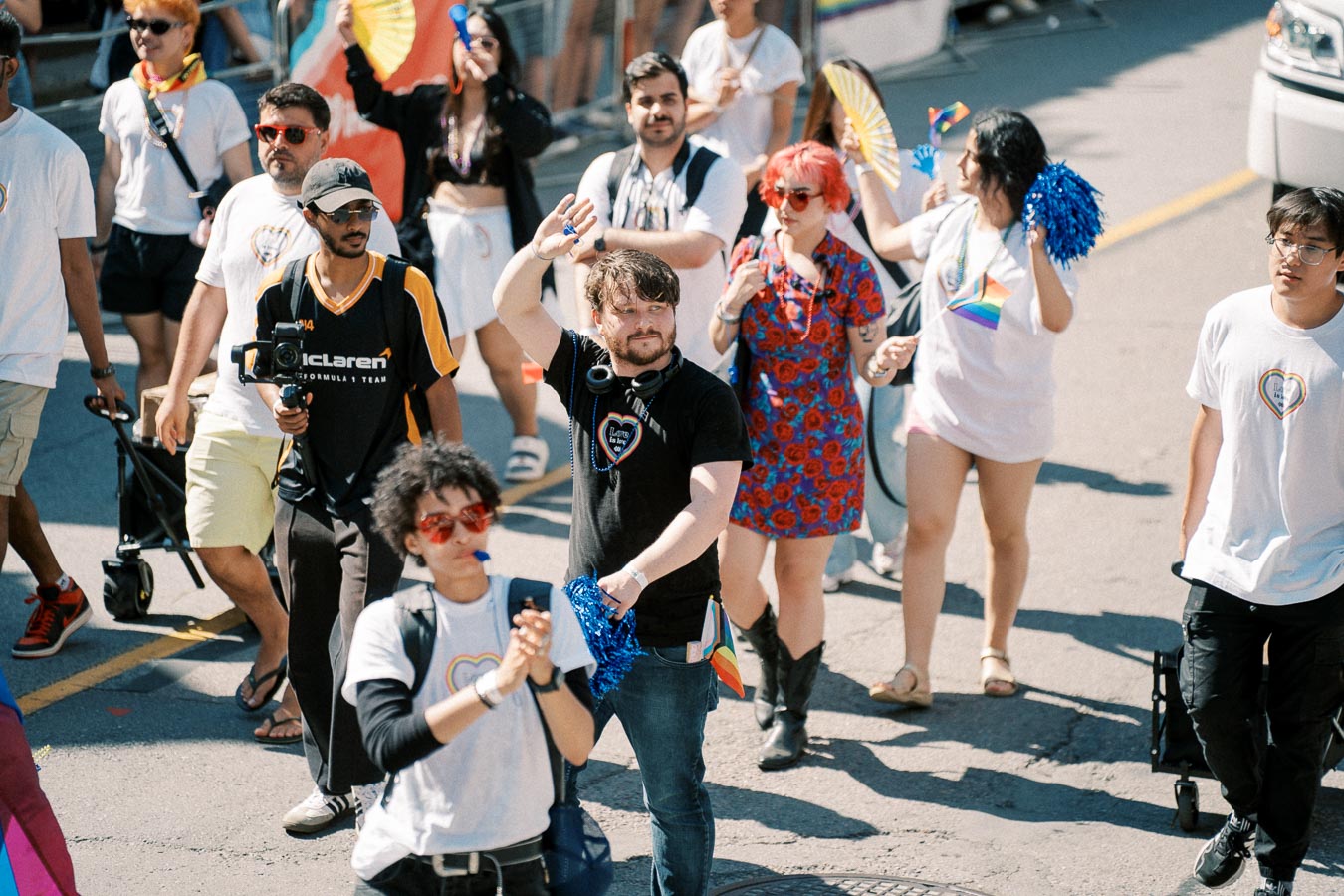 Participants in a parade walk down the street, displaying rainbow flags and pom-poms, celebrating diversity and inclusion.