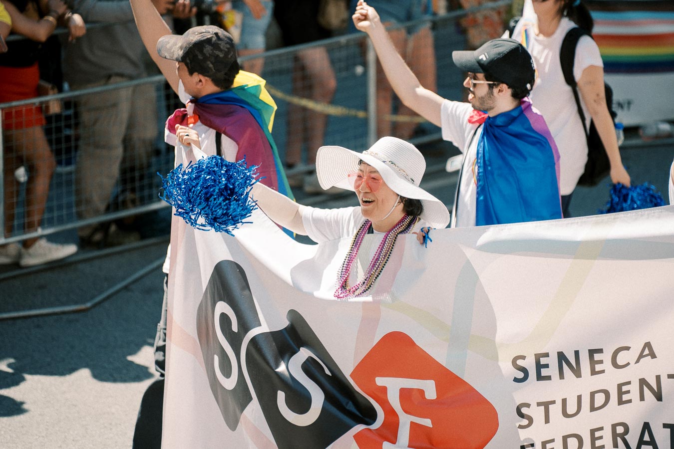 Participants in a parade hold a banner for the Seneca Student Federation, adorned with colorful accessories and waving to the crowd.