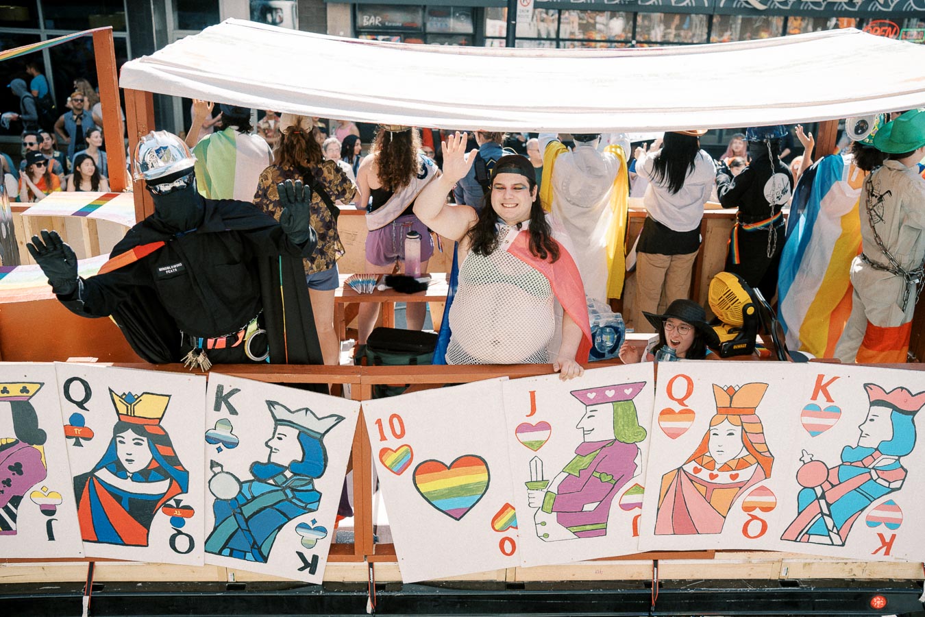 Parade float with pride-themed playing cards and participants in colorful costumes.