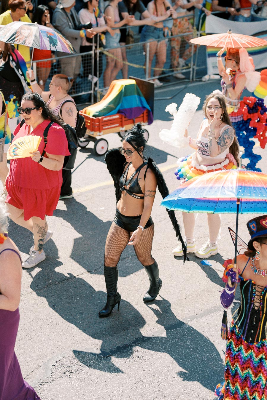Participants in a lively parade dressed in colorful costumes, carrying rainbow umbrellas and flags, celebrating diversity and inclusion.