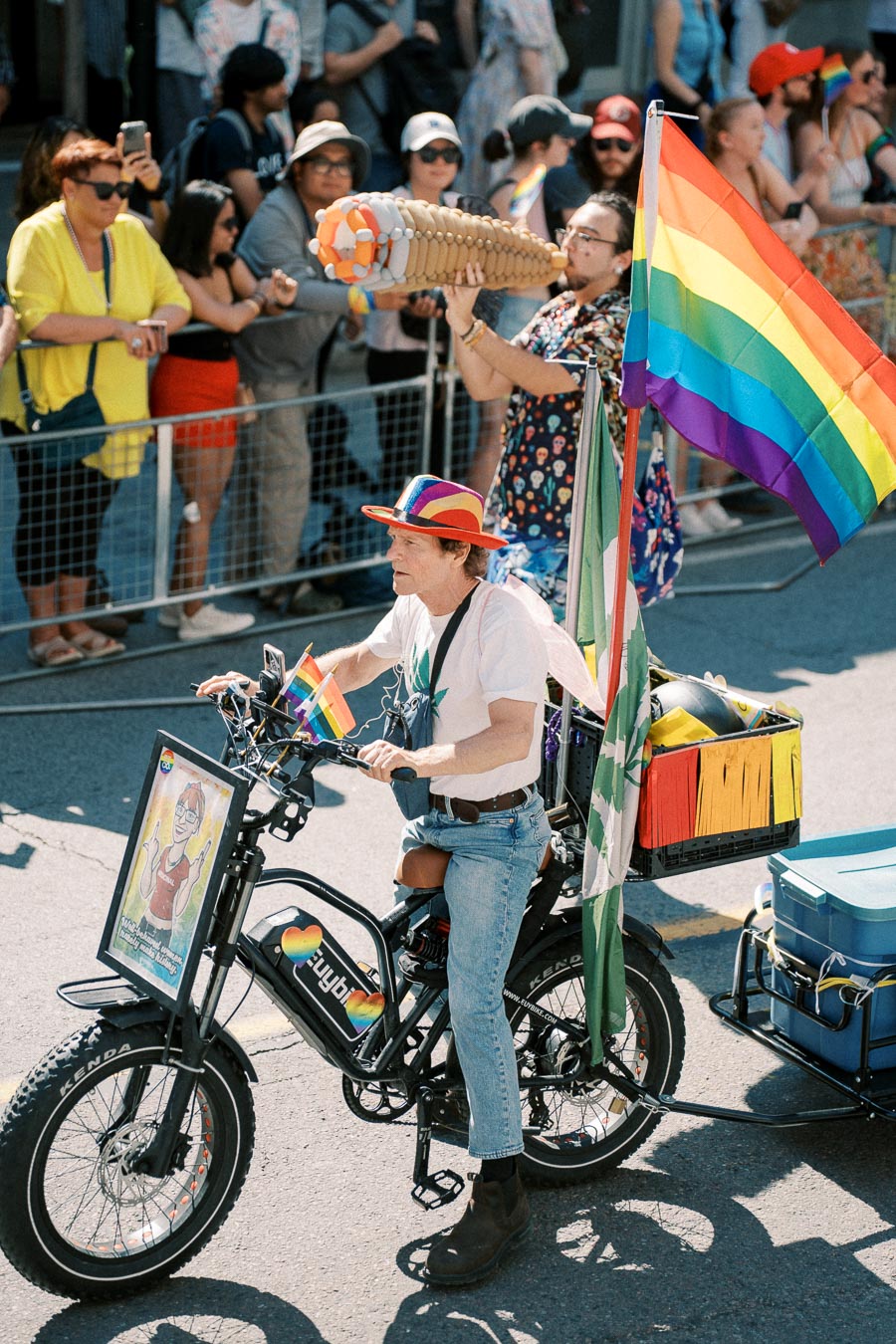 A participant rides an electric bike adorned with rainbow flags during a pride parade, engaging with the crowd.