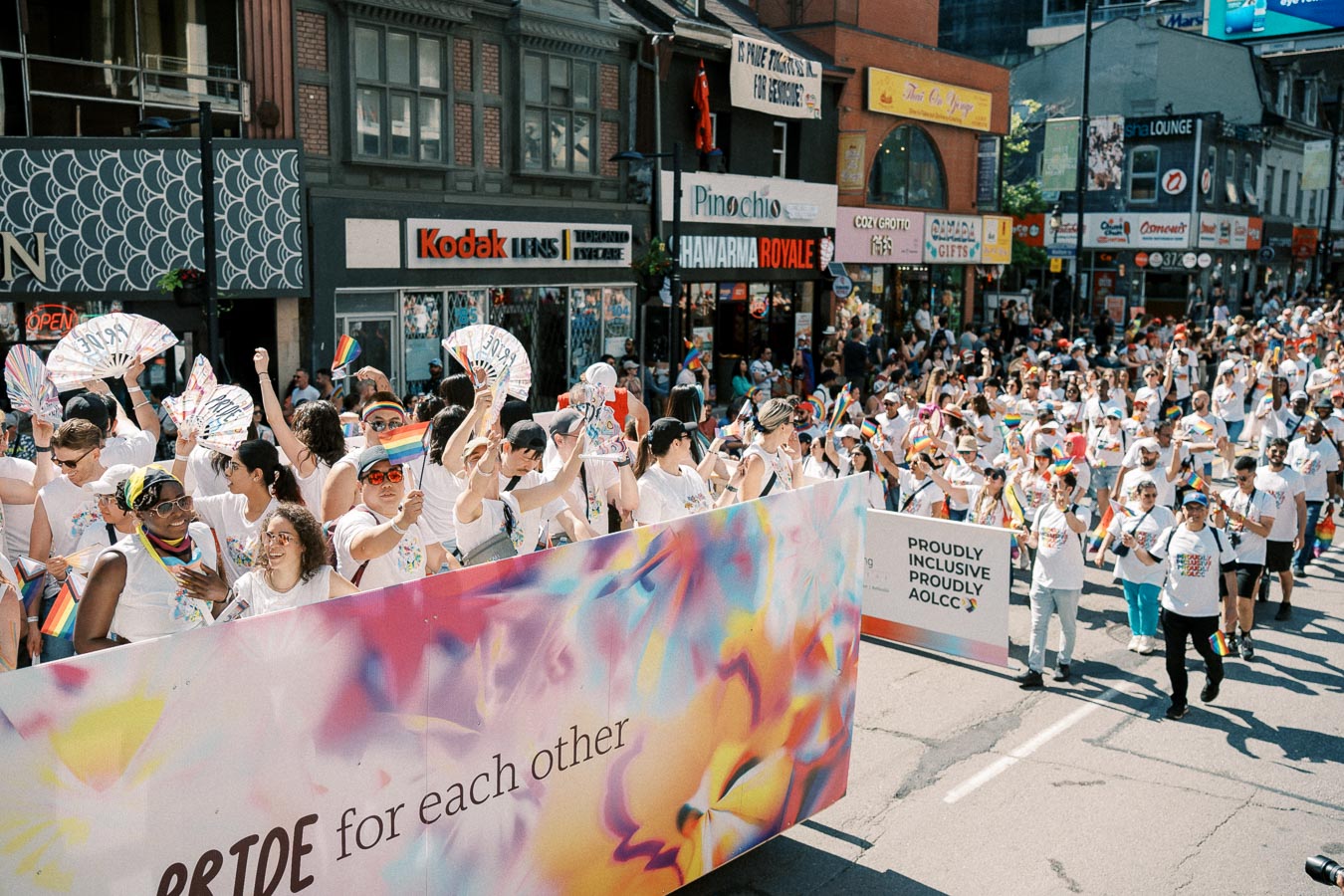 Participants in a pride parade march down a city street, holding rainbow flags and fans, celebrating diversity and inclusion.