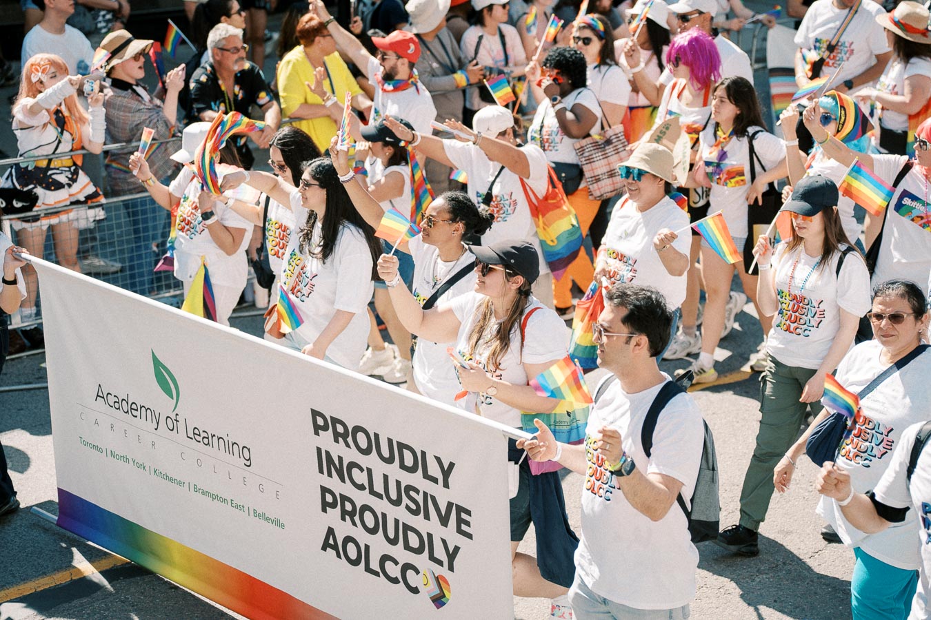 Participants from the Academy of Learning Career College march in a pride parade, celebrating inclusivity and diversity with rainbow flags and themed T-shirts.