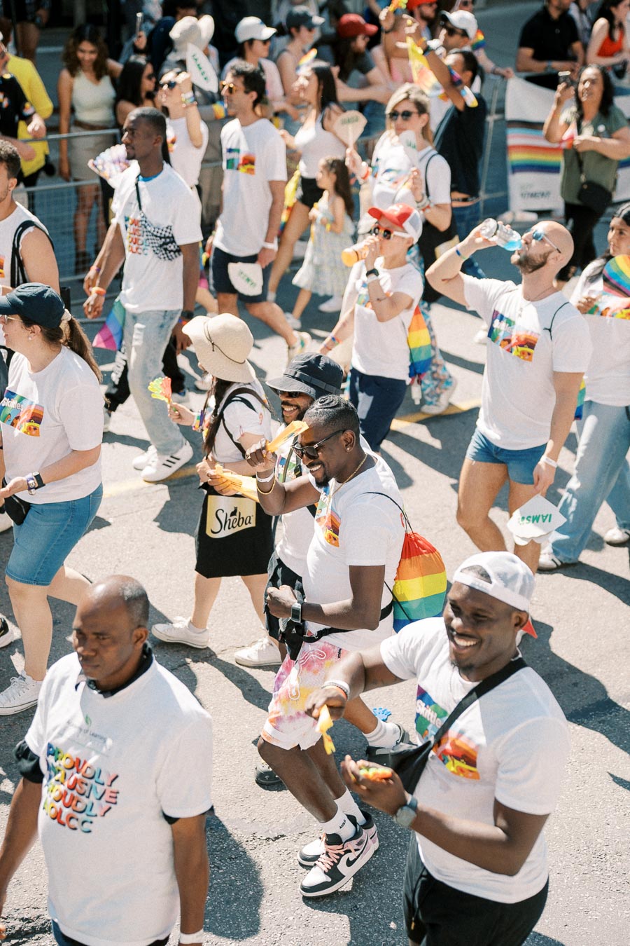 Participants in a pride parade wearing white shirts with rainbow designs, celebrating diversity and inclusion.