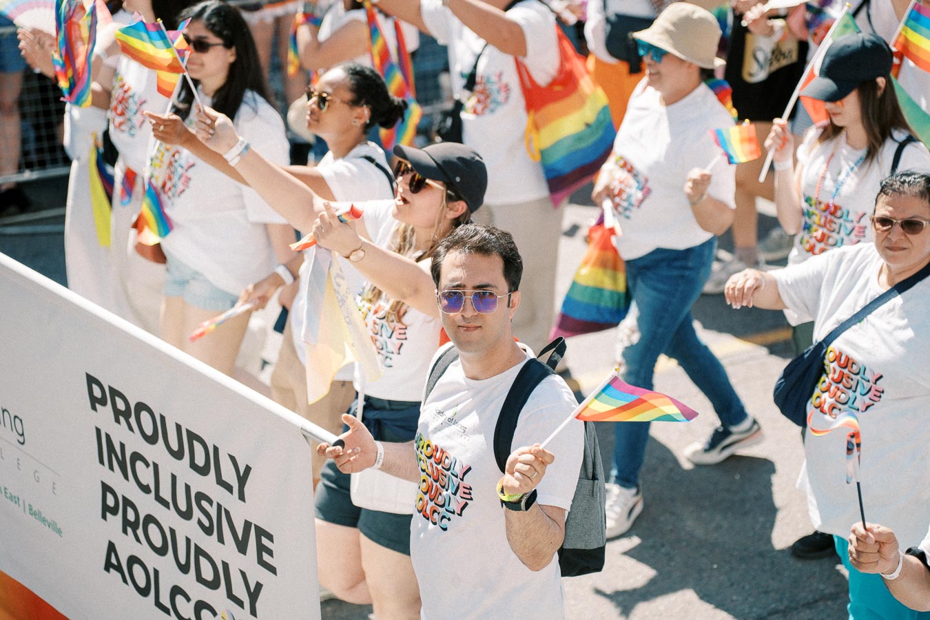 Participants in a pride parade celebrate diversity and inclusion, waving rainbow flags and wearing themed shirts.