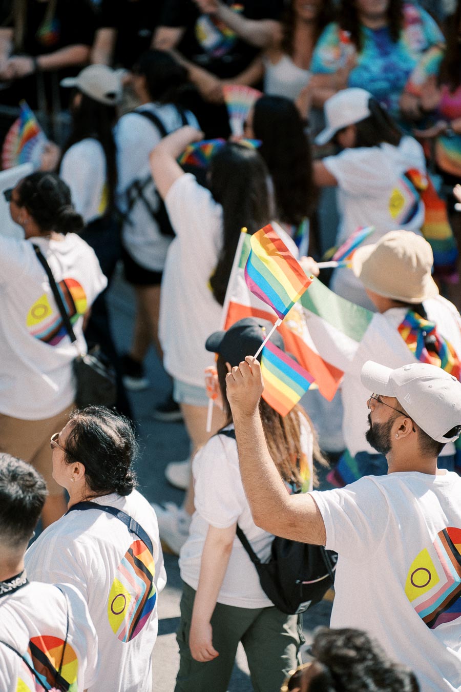 Participants in a pride parade wearing white shirts with rainbow designs and waving rainbow flags.