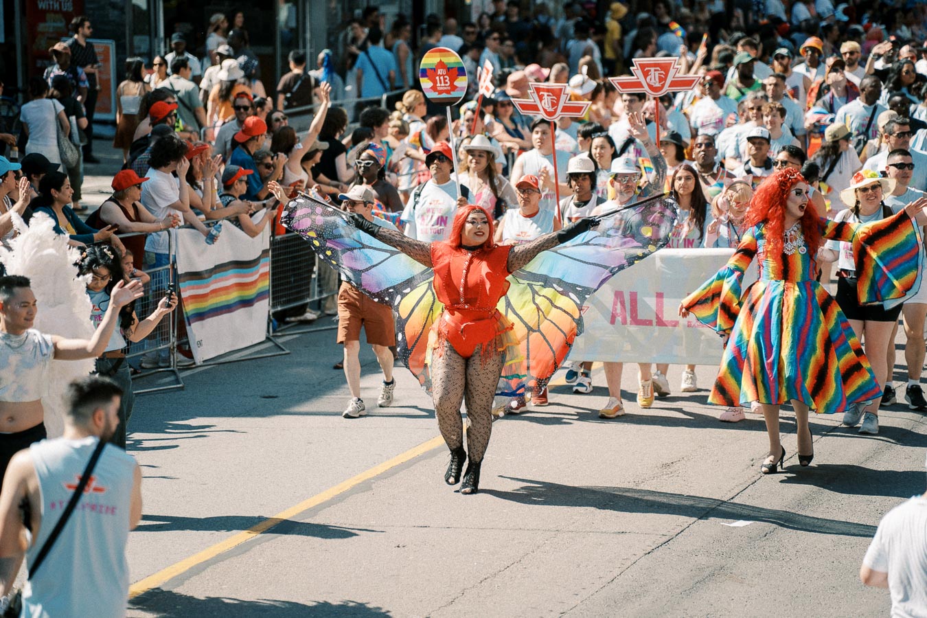 Participants in colorful costumes, including a butterfly and rainbow dress, celebrate at a lively parade.