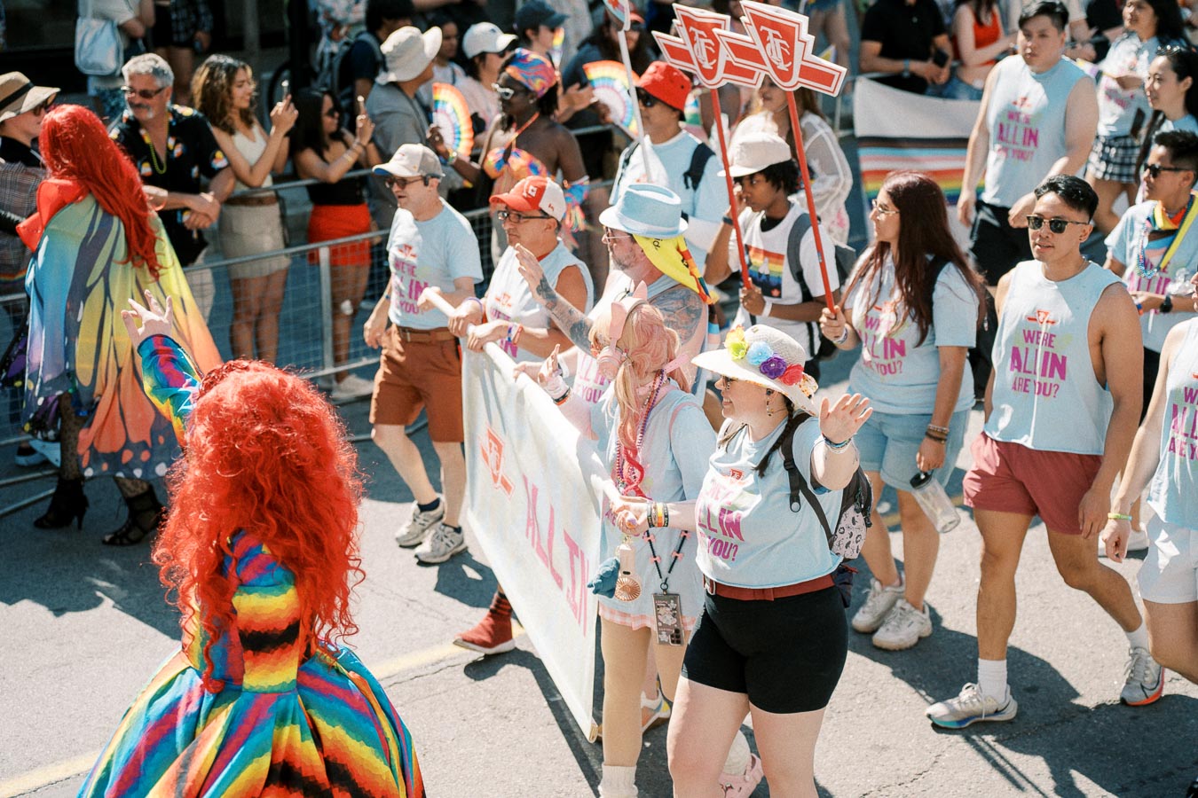 Participants in a pride parade march with colorful outfits and a banner, celebrating diversity and inclusion.