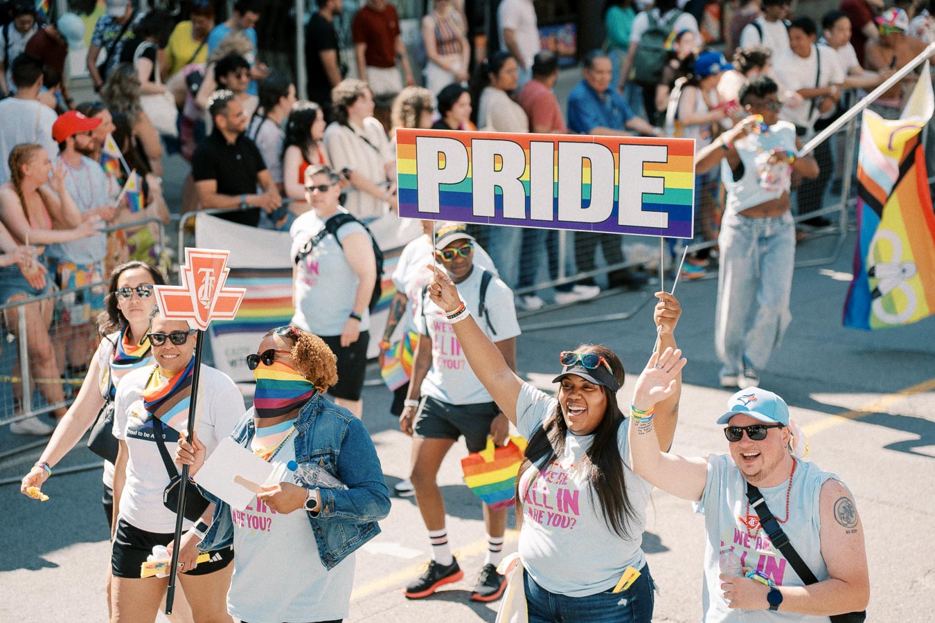Participants in a Pride parade joyfully march while holding a colorful 'PRIDE' sign, celebrating diversity and inclusion.