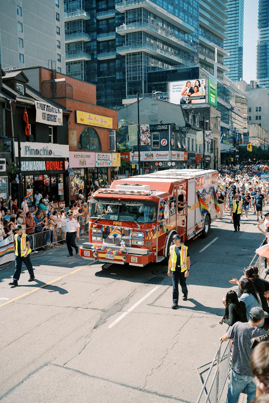 A decorated fire truck participates in a city parade, surrounded by crowds and urban buildings.